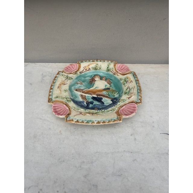 Square Majolica mermaid plate with shells on the corners, the mermaid sit on a flying fish, the border is decorated with...