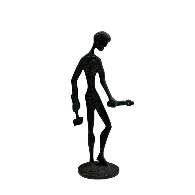 A striking vintage bronze sculpture depicting a highly stylized elongated human figure holding a hammer in one hand and a...