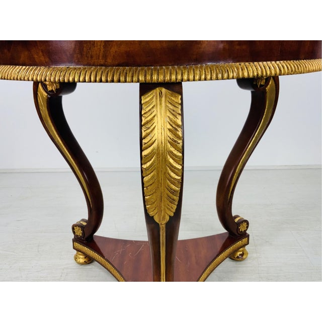 A vintage mahogany Regency style accent table with gilt finished carved accents, three hefty cabriole legs, triangular...