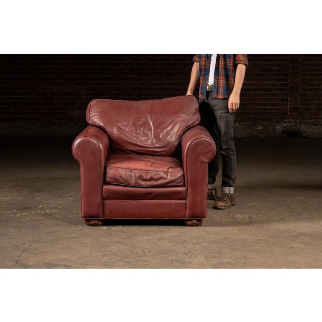 Richly upholstered red leather armchair paired with a matching ottoman, both set on turned wooden bun feet. The chair...