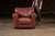 Richly upholstered red leather armchair paired with a matching ottoman, both set on turned wooden bun feet. The chair...