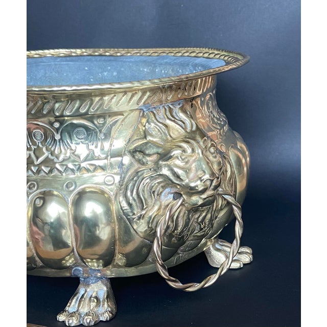 Elegant antique brass jardiniere featuring finely detailed lion head handles with suspended ring pulls and a richly...