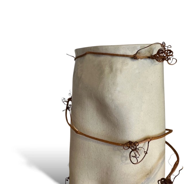 This handcrafted vase features a sleek silhouette with a sculptural vine or branch wrapping gracefully around its body....