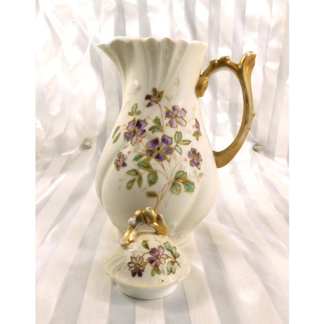 This is a white Jean Pouyat Limoges Chocolate pot. The right side has purple hand painted flowers with green leaves. One...