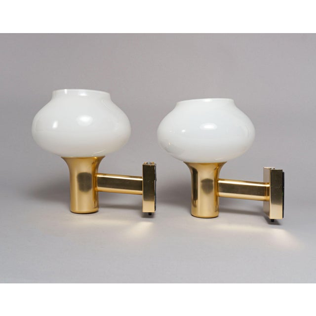 A pair of understated gold-coloured wall lamps with polished metal bodies, slightly upwards-tilted stems, flared rims and...