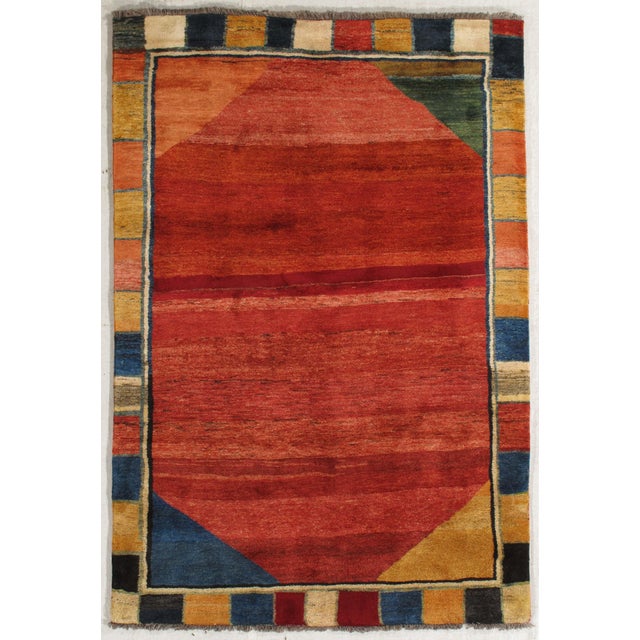 Vintage Hand-knotted Persian Gabbeh rug featuring a large central geometric field in tonal red hues, framed by a...