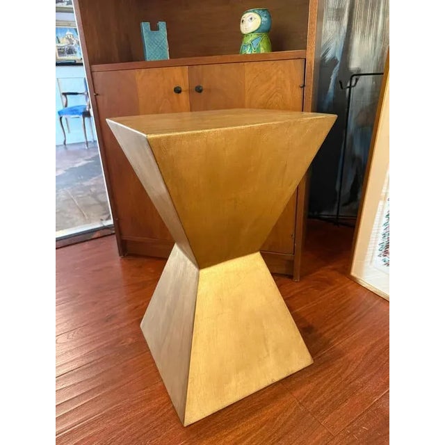 This contemporary pedestal features a bold double-pyramid silhouette finished in luminous antique gold on metal. Its...