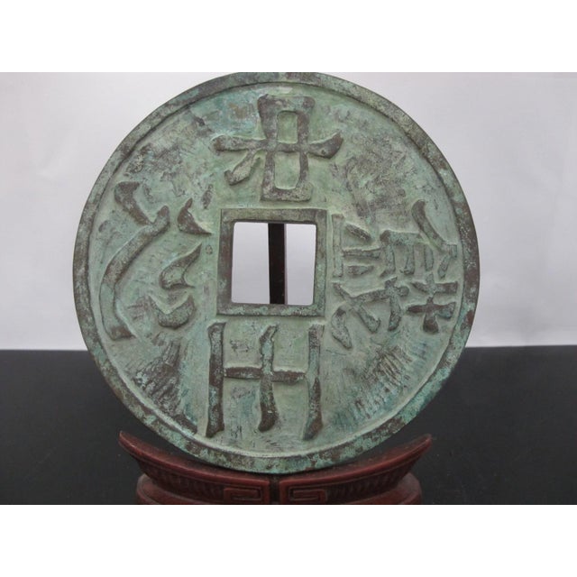 Large antique East Asian cash coin on carved wood stand. Chinese "Dà Zhōng Tōng Bǎo in bronze metal with aged green...