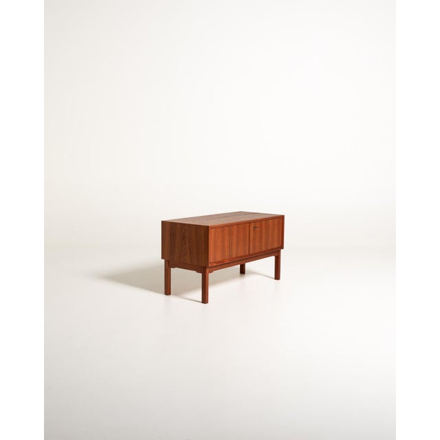 Scandinavian low teak sideboard from the 1960s, with two doors, a brass lock, and a frame base with square legs....