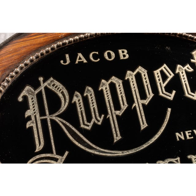 Antique reverse-painted glass and silver-foil advertising sign for Jacob Ruppert's Beer of New York. The oval sign...