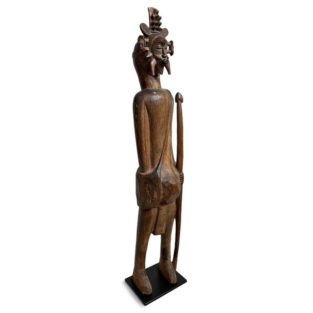 Antique hand-carved hardwood Senufo sculpture depicting a standing male hunter figure adorned with an elaborate ceremonial...
