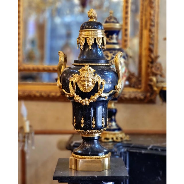 Elegant French Empire-style decorative urn crafted in rich black porcelain and embellished with elaborate gilded bronze...