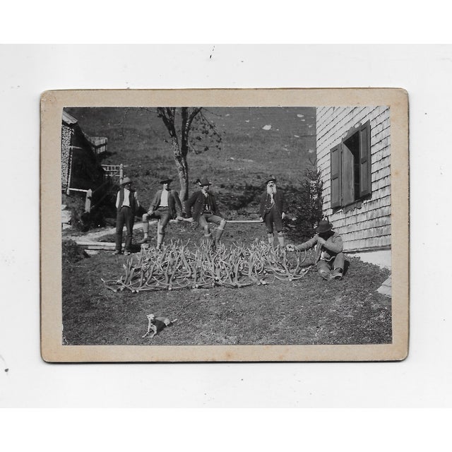 Antique Swiss or German black and white photo of men in lederhosen and a dog posing with antlers. Possibly they are hunters.