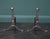 A pair of English mid-19th century polished wrought fire dogs. Wrought uprights with rivets on arched supports with penny...