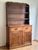 Rustic farmhouse-style hutch cabinet in solid wood with a warm, medium-tone finish. The upper section features open...