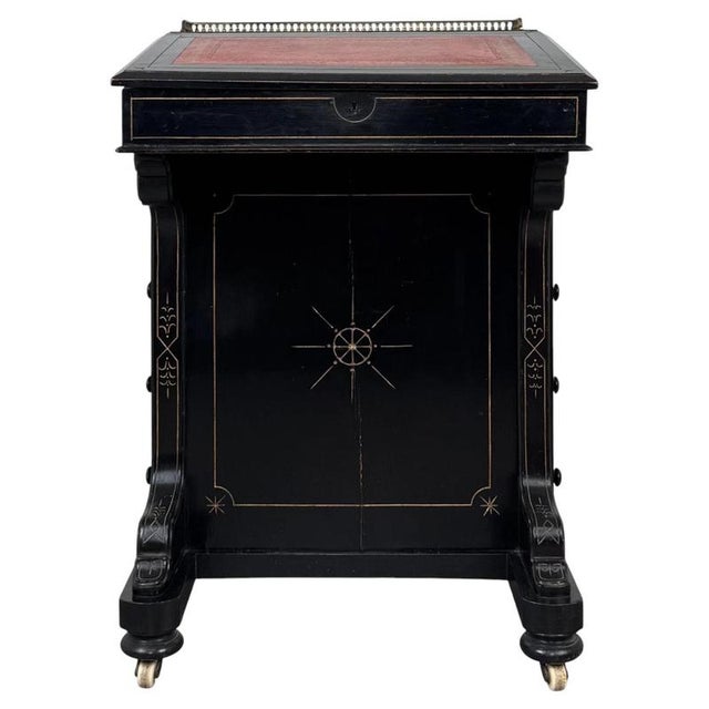 A refined 19th-century English Davenport desk, distinguished by its dramatic ebonised finish, rich red leather writing...