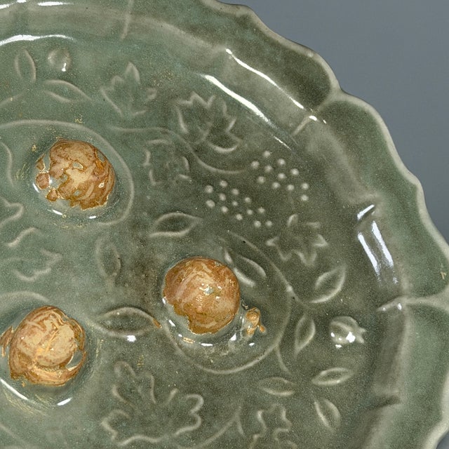 This is a handmade Longquan celadon plate with scalloped flower‑form rim. Relief‑carved pattern decorates the inner...