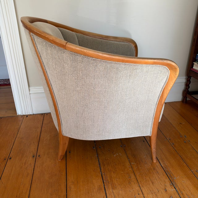 A sculptural barrel chair with a solid maple frame. The top rail sweeps into curved arms that taper down into slender...