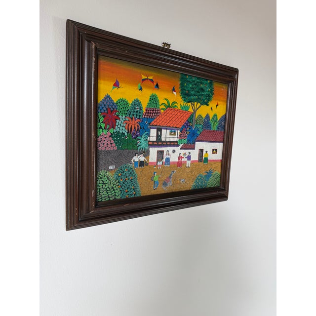 A vibrant 2003 folk art oil on canvas painting by Jadiro, depicting a lively village scene surrounded by lush tropical...