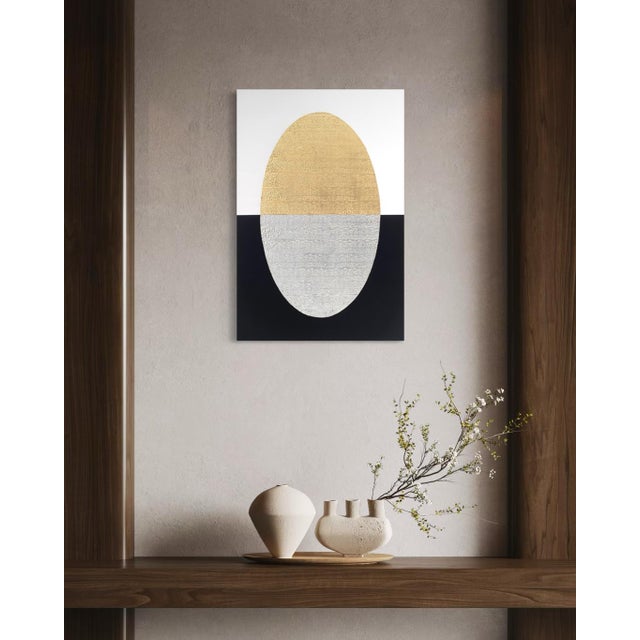 A glowing, gold-leafed oval rests atop a composition split cleanly between white above and black below, the metal leaf...