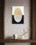 A glowing, gold-leafed oval rests atop a composition split cleanly between white above and black below, the metal leaf...