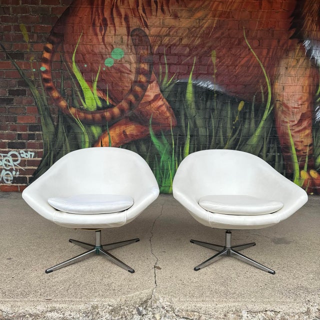 Pair of mid-century modern swivel chairs by Overman. These chairs feature a white vinyl and chrome bases. There is an...