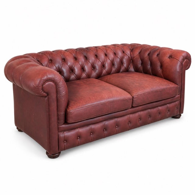 Handsome leather Chesterfield sofa featuring deep button tufting, iconic rolled arms, and two generous seat cushions. The...