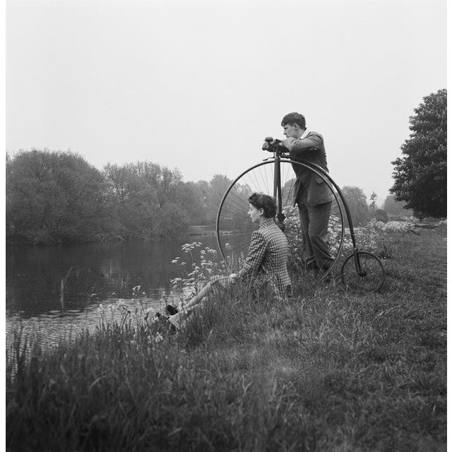 A Day on the River A young couple with a penny-farthing relax on the banks of the River Thames near Eton, Berkshire, July...
