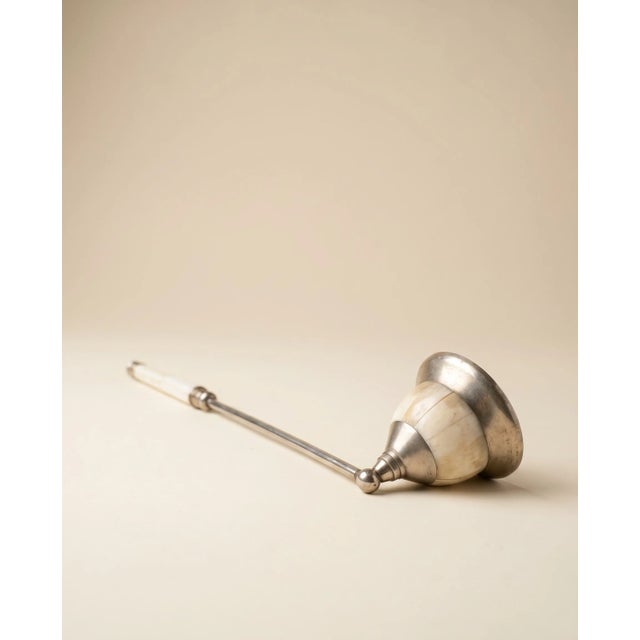 Elegant vintage candle snuffer featuring a long metal shaft, a sculpted bell-shaped snuffer head, and a segmented white...