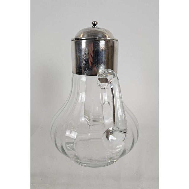 Elegant Italian pitcher produced during the 1950s, combining hand blown glass with a silver-plated mount and hinged lid....