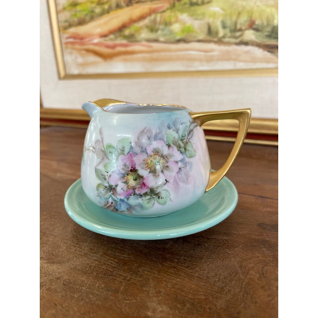 This vintage creamer and saucer set features a delicate hand-painted floral motif in soft pastel tones. The creamer has a...