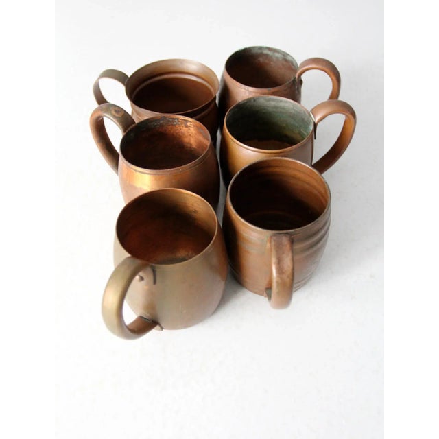 Set of six vintage solid copper mugs, circa 1930–1950, featuring classic cylindrical forms with rounded handles. This...