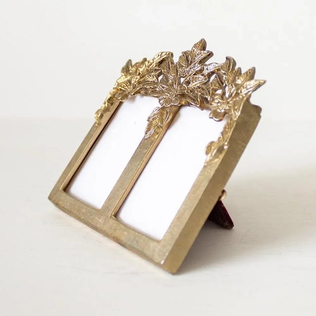 Small Victorian-style brass tabletop double picture frame features floral crown across the top and two small spaces for a...