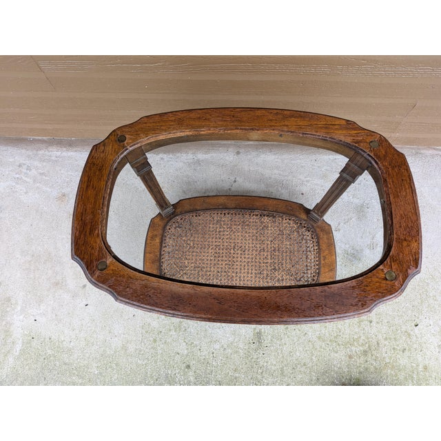 This is a vintage two tier oval end table featuring a glass top, wood frame, and a woven can lower shelf. Could be placed...