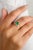 This exquisite wedding ring features a stunning 0.08 carat pear-cut green emerald, complemented by shimmering diamonds...