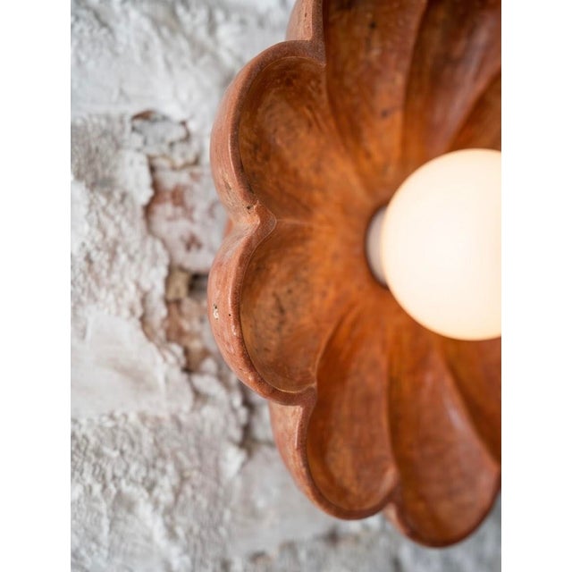 A sculptural wall sconce hand-carved from a single block of natural red travertine. Soft, rounded petals frame a frosted...