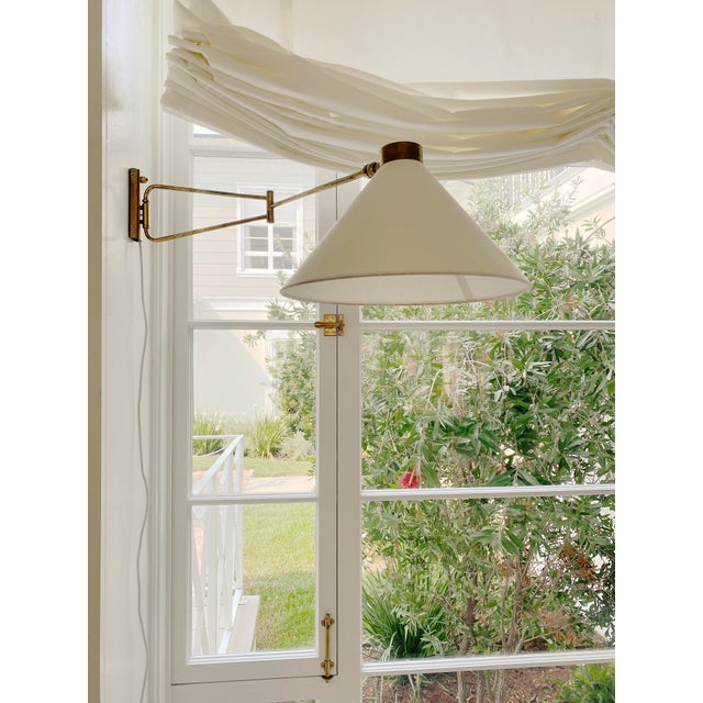 1970s Mid Century Modern French brass swing arm wall sconce featuring a white linen shade. The brass arm extends and...