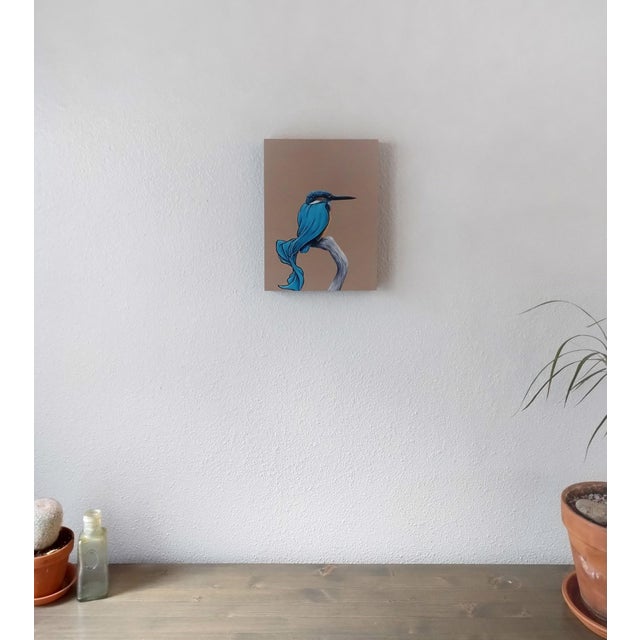 This artwork depicts a kingfisher perched gracefully on a branch, adorned with flowing, cape-like drapery in vibrant...