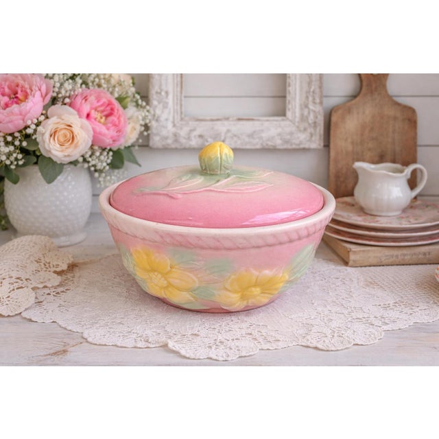 A charming vintage covered dish by Hull Pottery, featuring a soft pastel pink ground with hand-applied yellow floral...