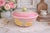 A charming vintage covered dish by Hull Pottery, featuring a soft pastel pink ground with hand-applied yellow floral...