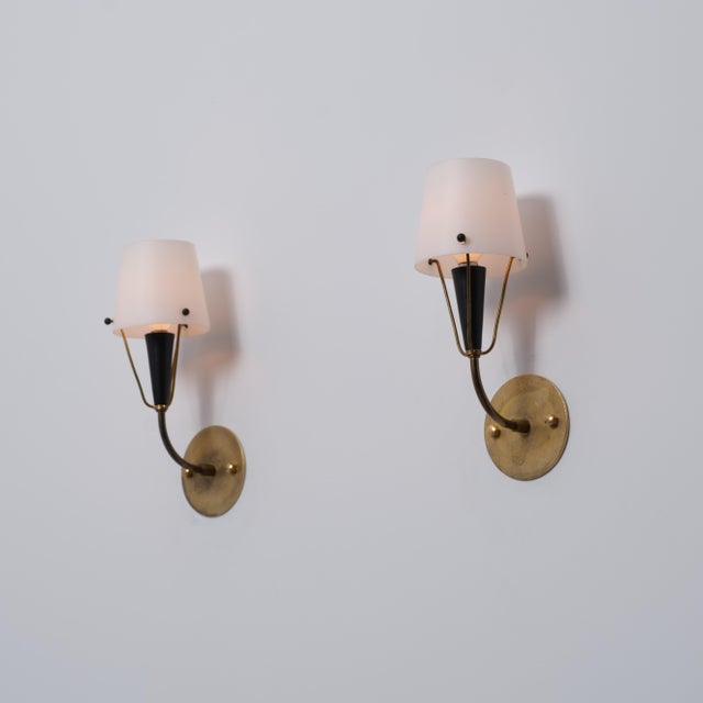 Pair of italian wall sconces from the 1950s, featuring round brass wall plates, gently curved brass arms, black lacquered...