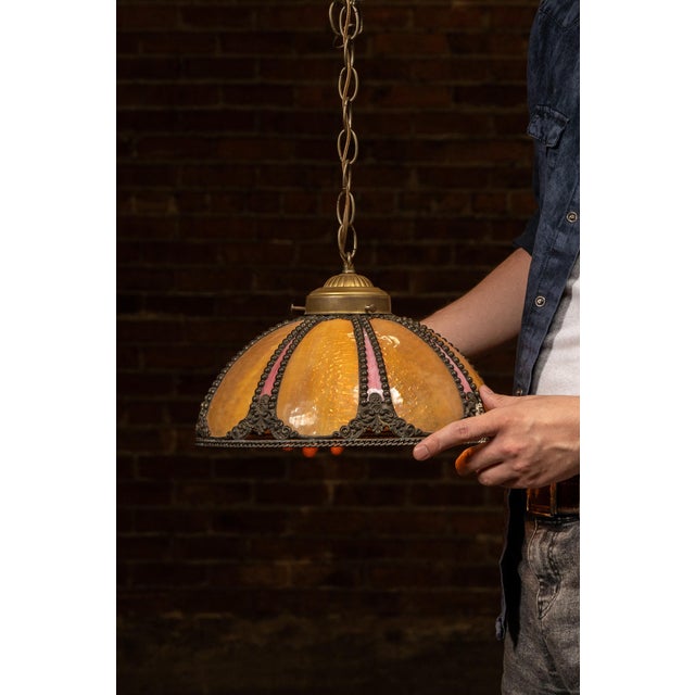Domed slag glass hanging pendant lamp with alternating amber and rose-hued glass panels set into a decorative cast metal...