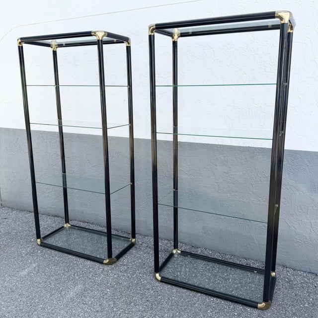 A striking pair of Art Deco–inspired étagères featuring glossy black lacquered frames accented with polished gold-tone...