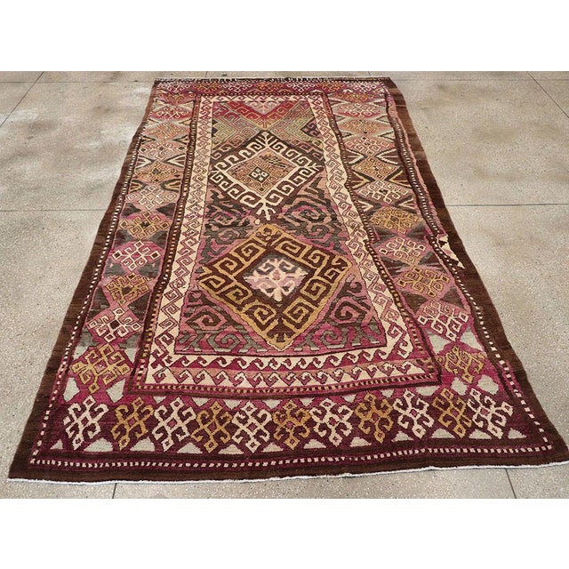 This early 20th-century Persian Kurdish accent rug presents a bold tribal composition in deep brown, magenta, rose,...