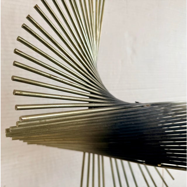 Sculptural mid‑century metal rod form in the manner of Curtis Jere, dramatically fanning out over a cylindrical stone...