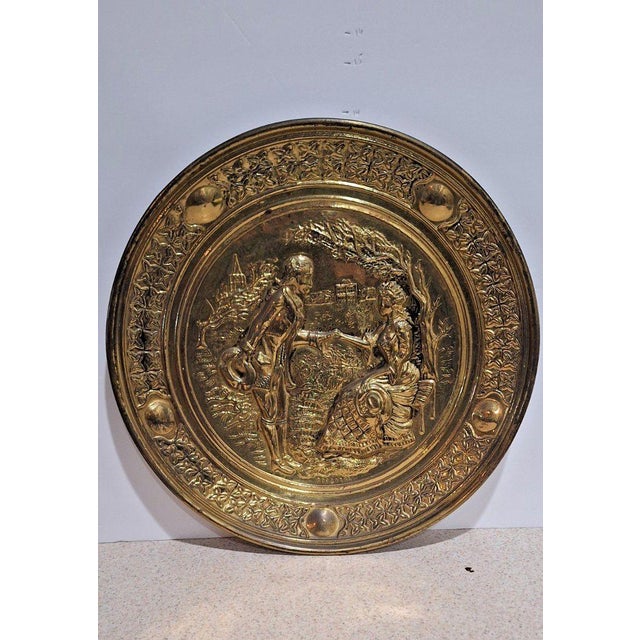 A pair of round brass repoussé wall plaques, each hand-worked in relief depicting a different courtship scene with figures...