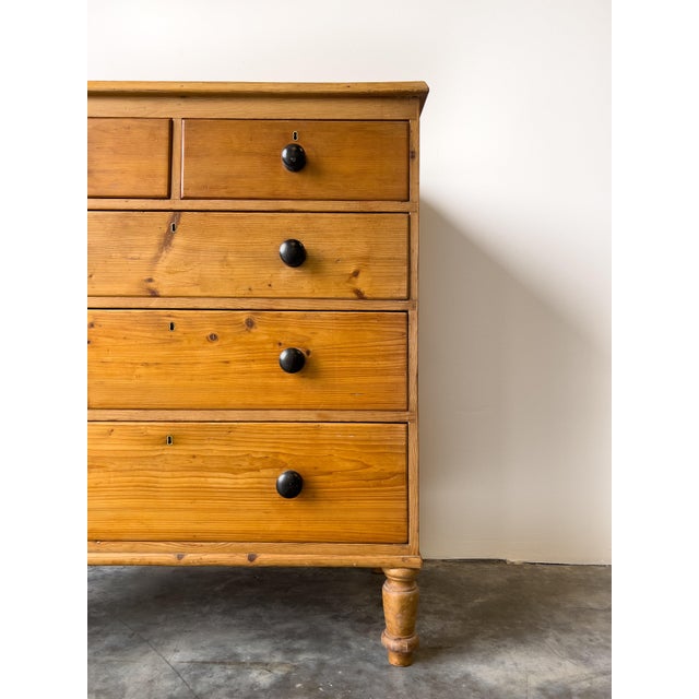 An antique Georgian English pine chest of drawers. Two short drawers over three long drawers with black knobs, on turned...
