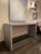 Waterfall console table wrapped in a textured grey fabric with silver nail heads. Designed and manufactured by Arden Home...