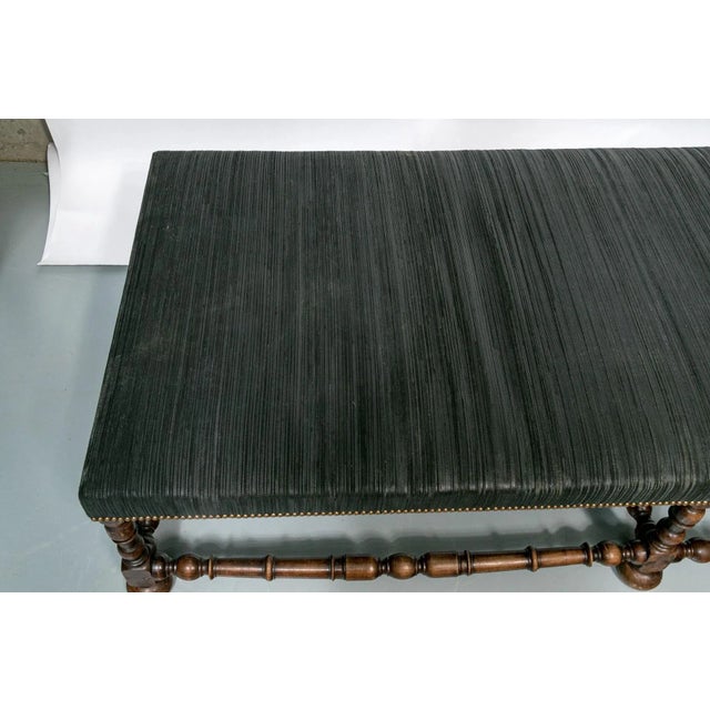 A large Jacobean style bench upholstered in a high quality durable and dark colored fabric with brass nailheads and six...