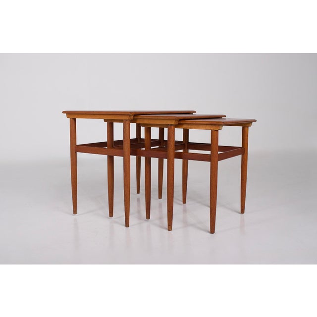 1960s: Three nesting teak coffee tables in Scandinavian style. A sliding mechanism is integrated under the tabletop to...